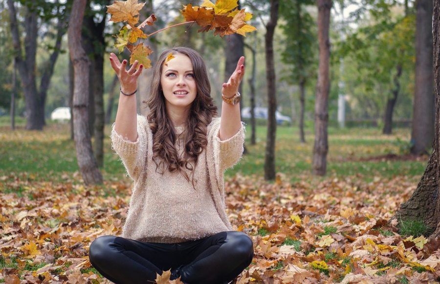 person sitting outside among fallen autumn leaves throws a bundle of leaves in the air, unwind this autumn