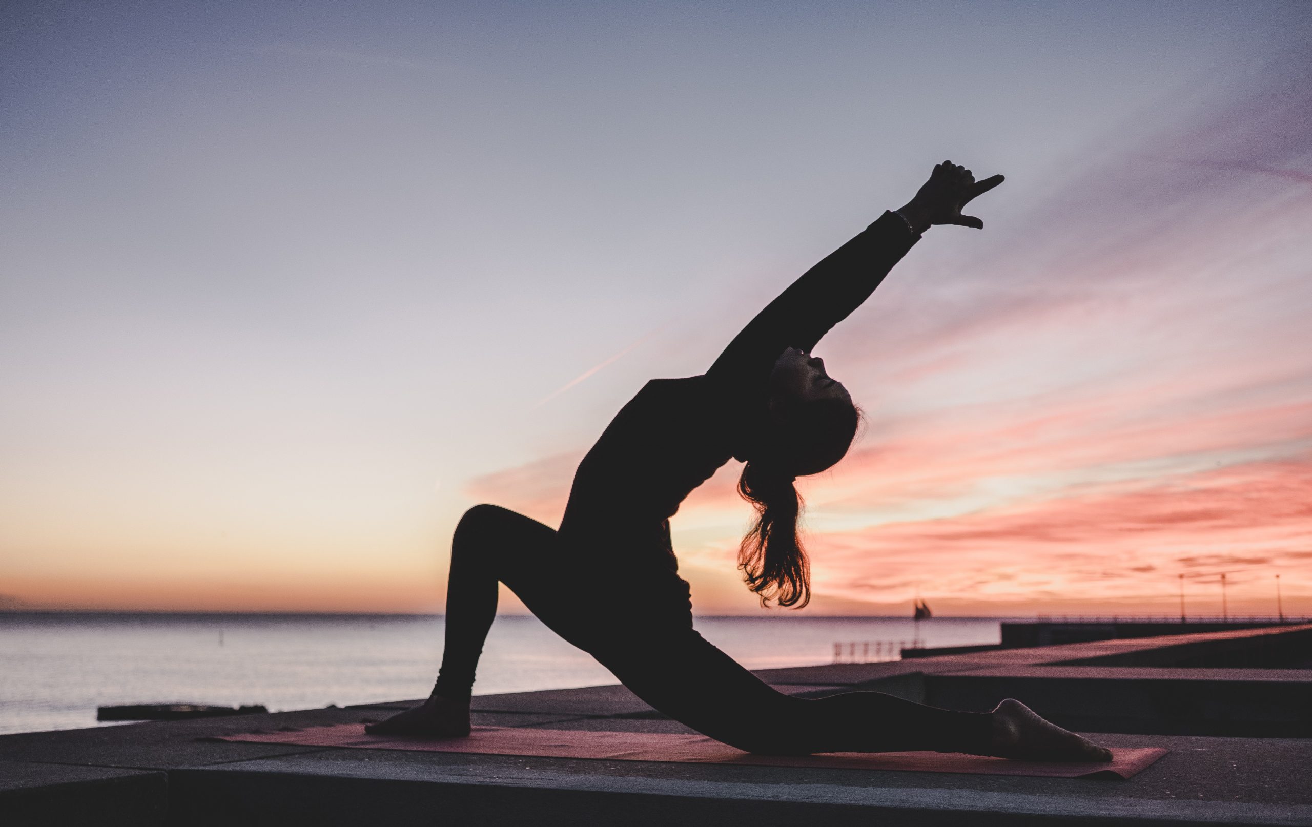 person doing yoga by water at sunset