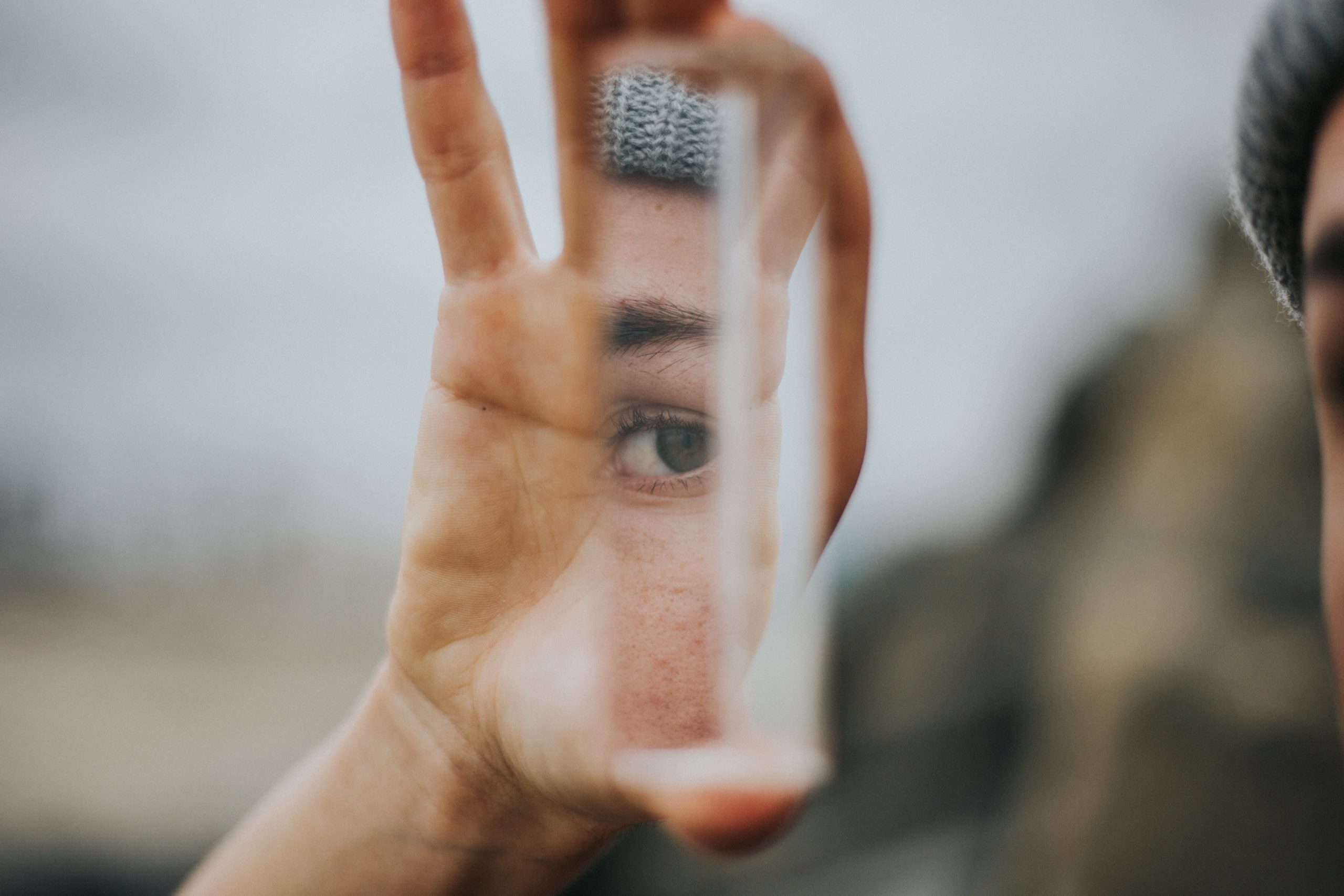 Person holding up small mirror shard, reflecting their eye