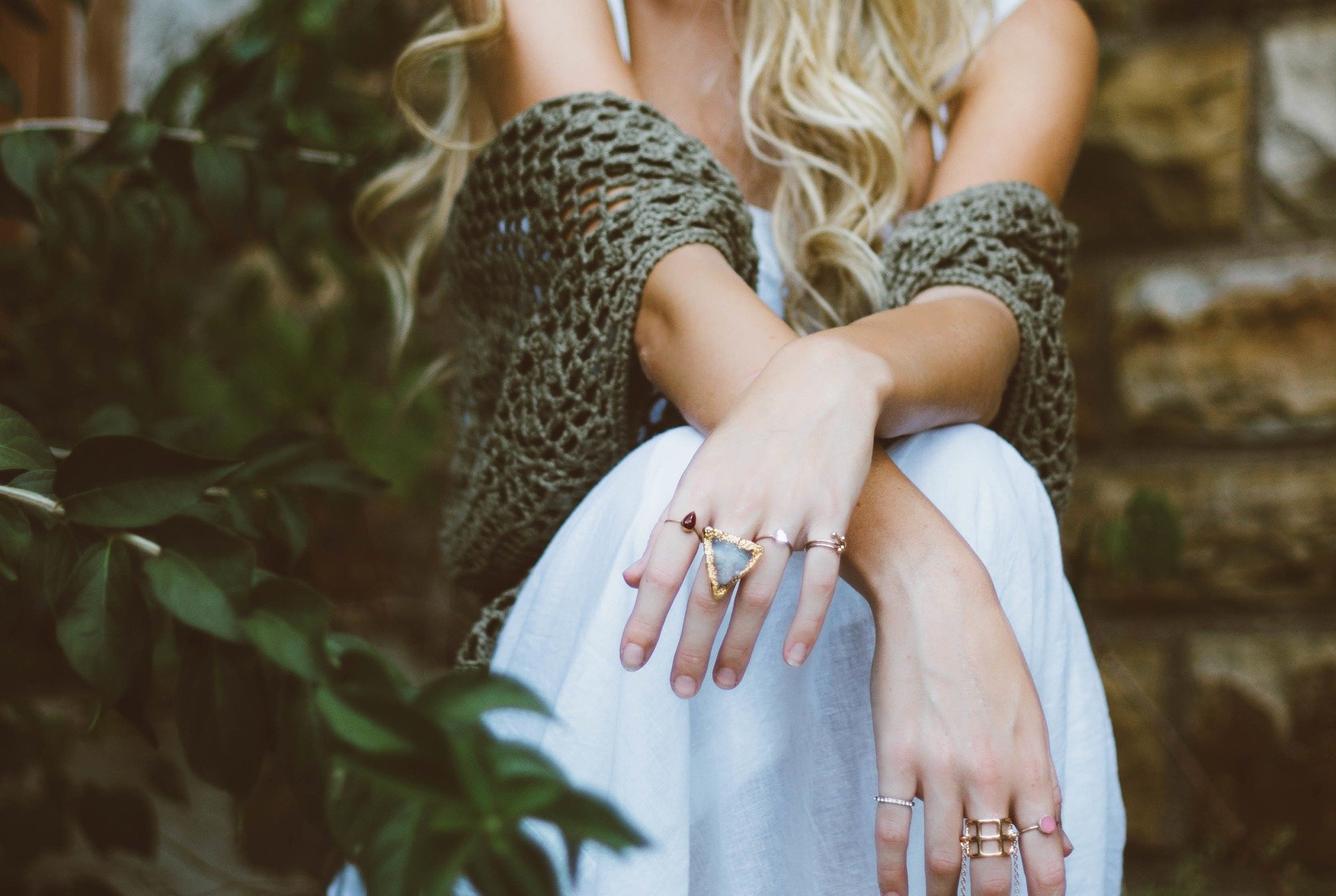 closeup of person's hands crossed over knees, wearing rings, youthful, sitting beside plants, anti-ageing for hands