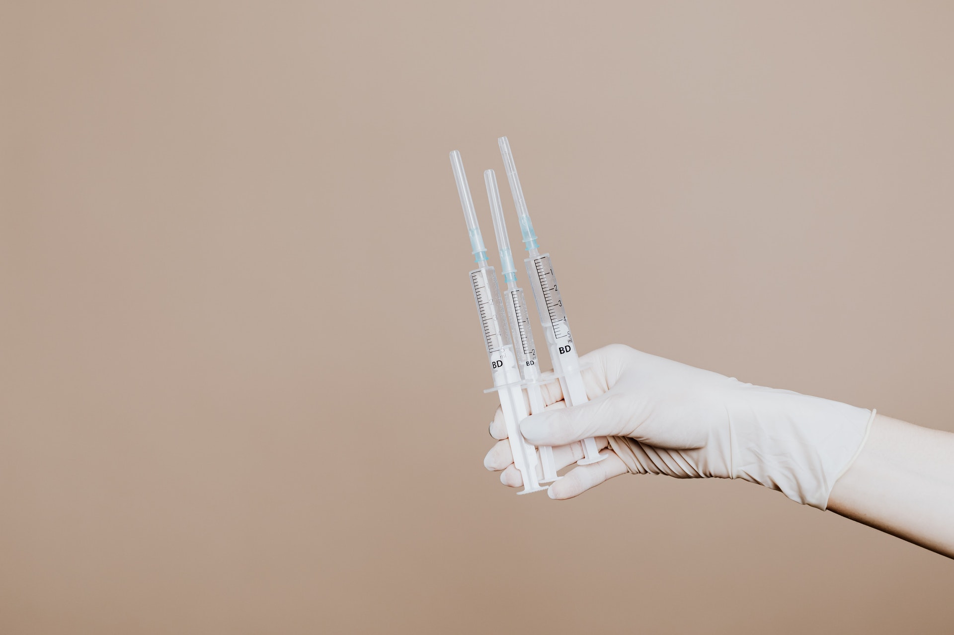 gloved hand holding hypodermic needles against plain backdrop