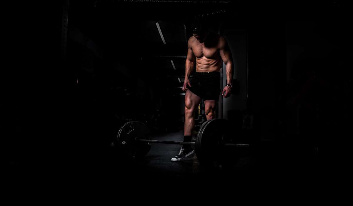 Shredded man looks down at weights, dark and moody background