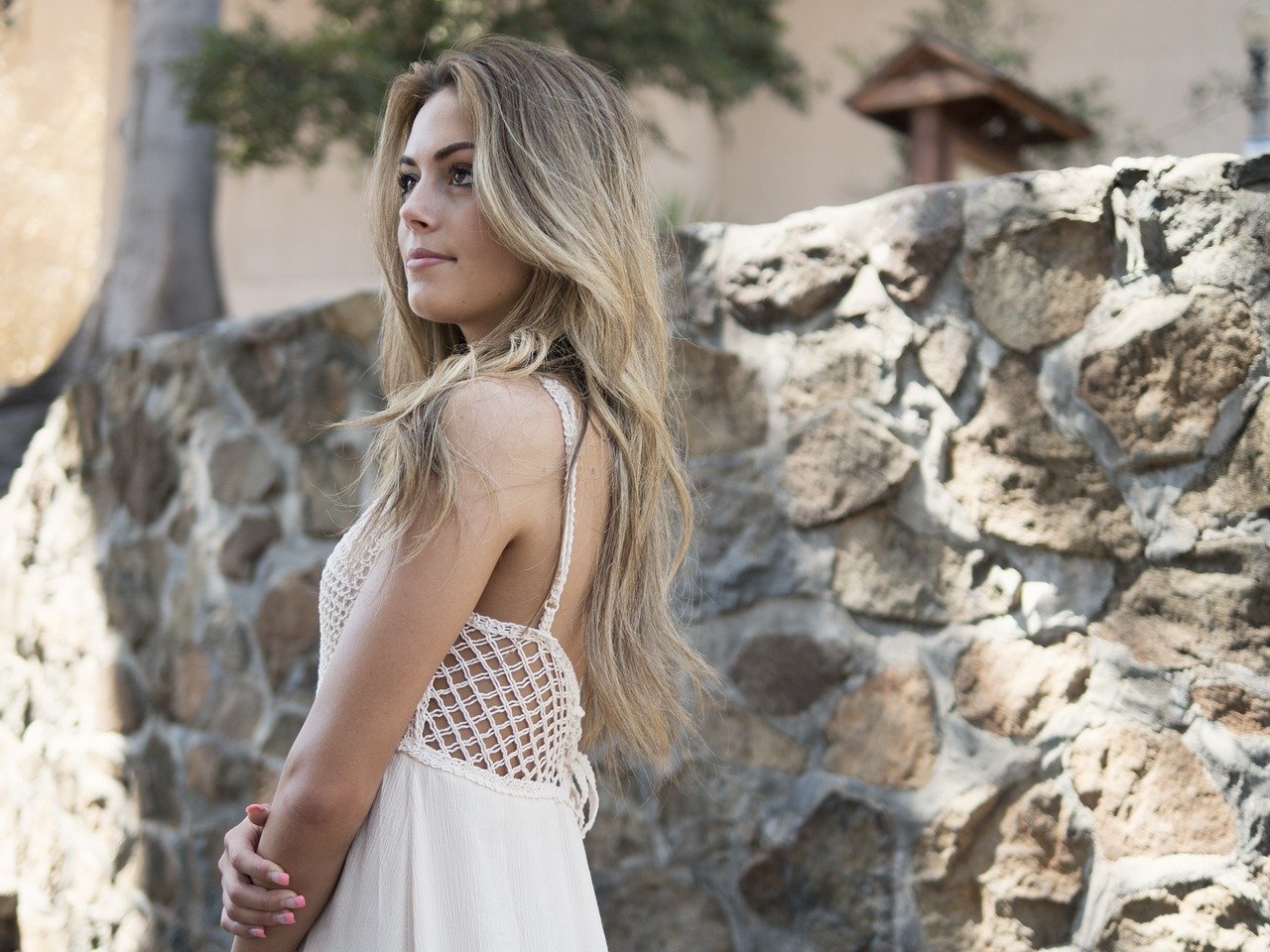 model standing outside in front of rural stone wall, facing off-camera, healthy skin