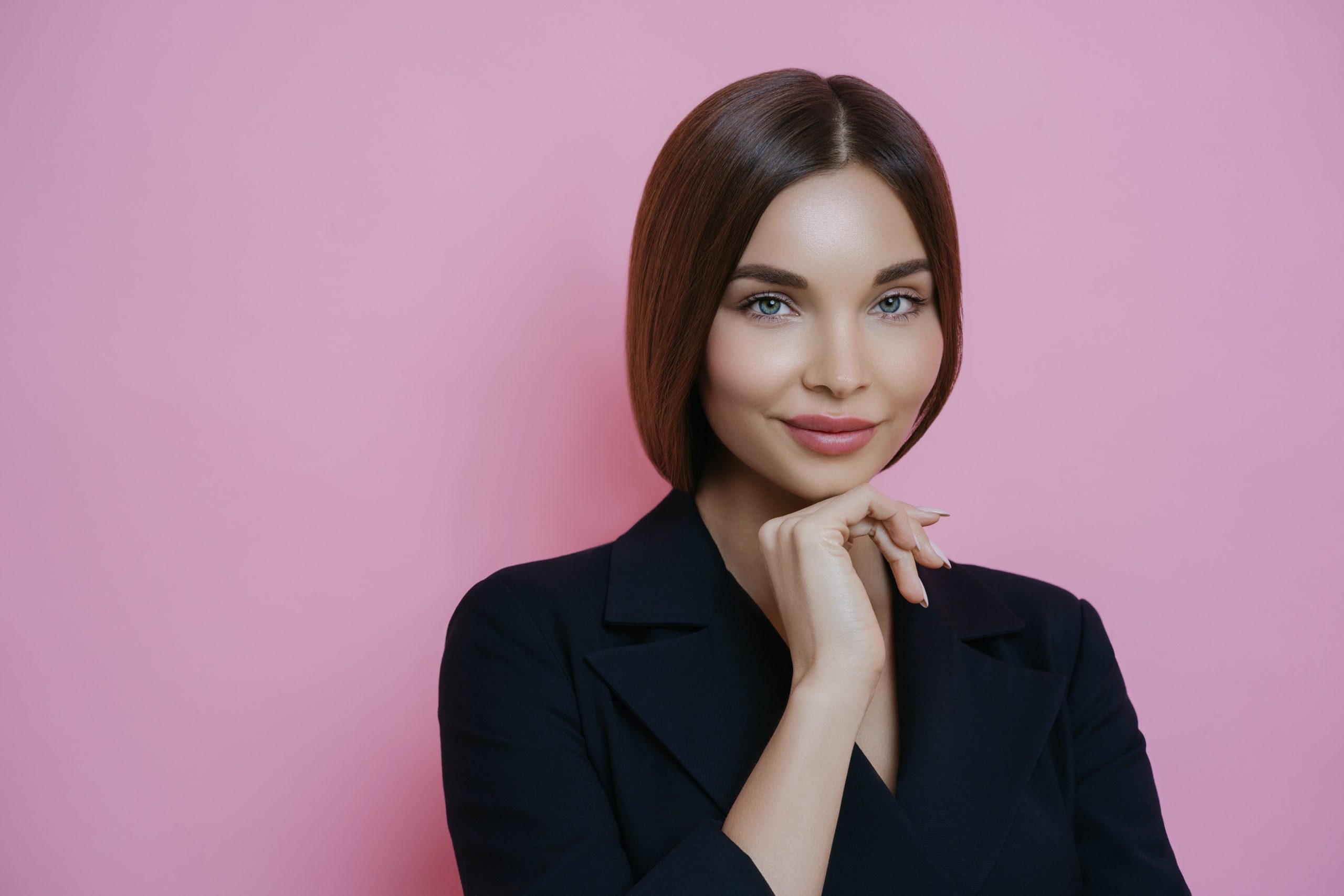 female model with smooth skin, hand on chin, pink background