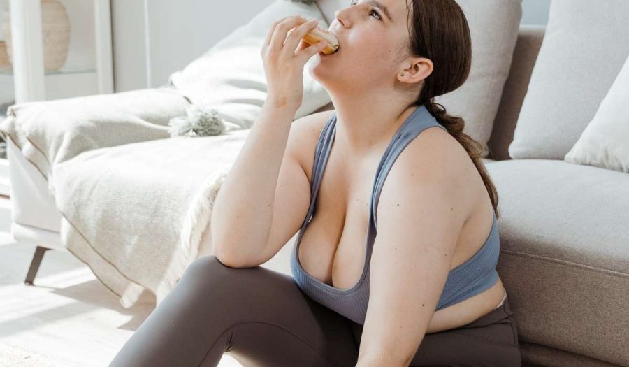 Person sitting on floor next to couch, wearing exercise clothes, eating a doughnut