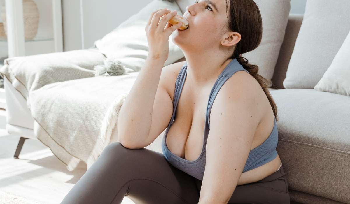 Person Sitting On Floor Next To Couch, Wearing Exercise Clothes, Eating A Doughnut