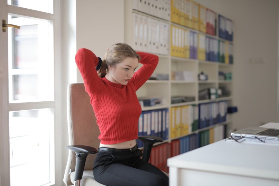 person sitting at home-office desk, tying hair back, laptop pushed to the side, ready to exercise from desk