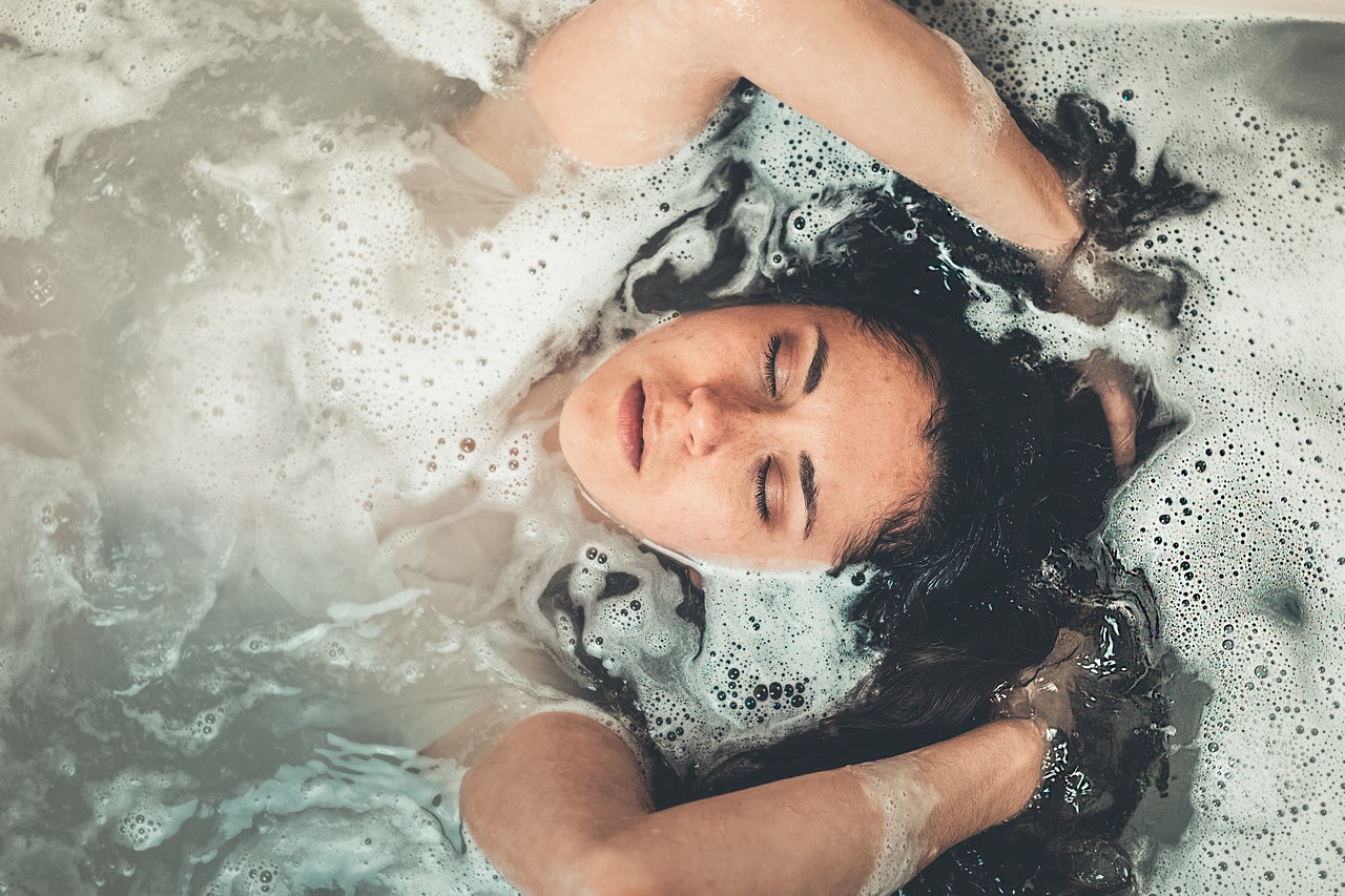 person lying in foamy water, hands up in hair, hard water and your skin