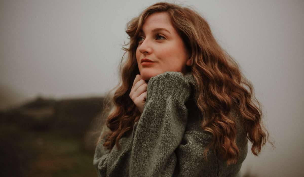 Person wearing a comfy sweater looks thoughtfully off-camera, outside against grey sky