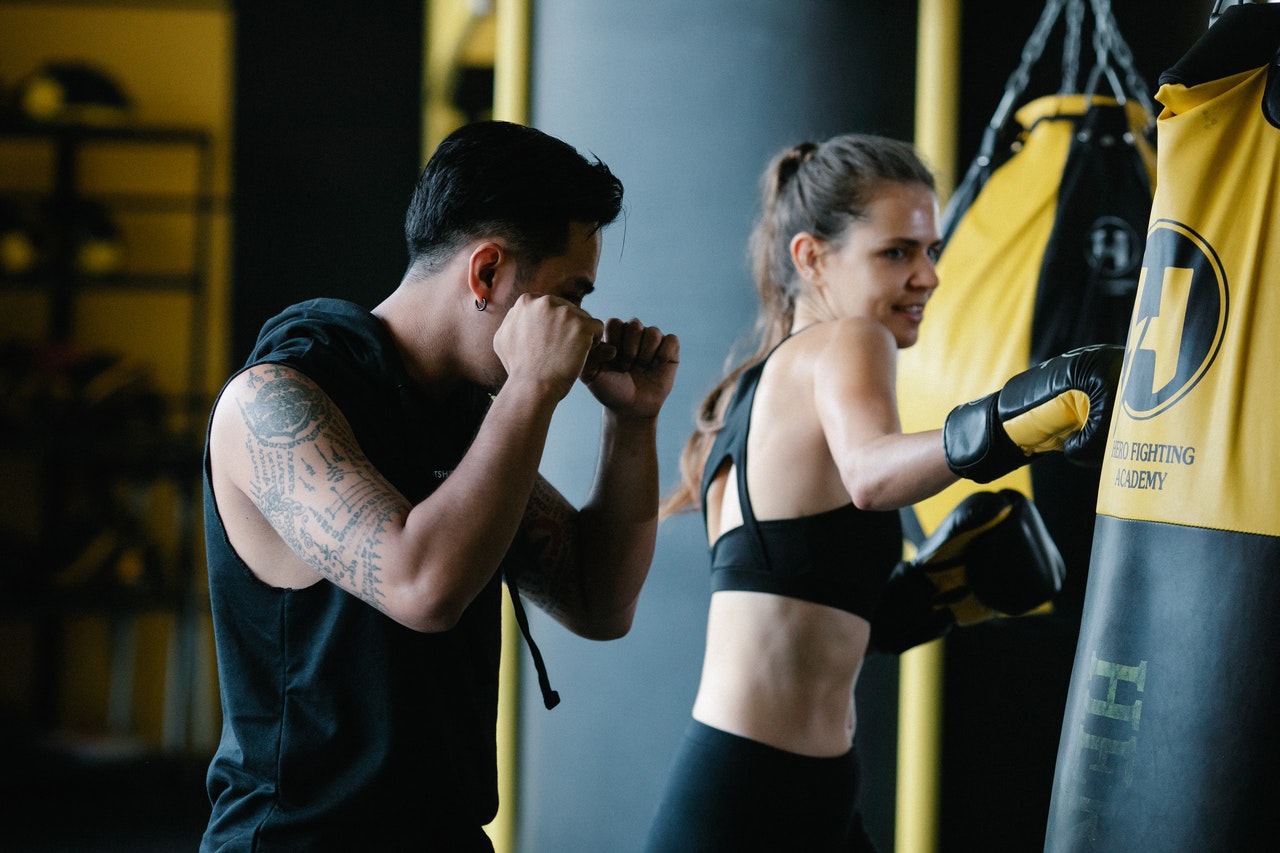 fitness trainer showing person how to properly punch boxing bag in a gym setting
