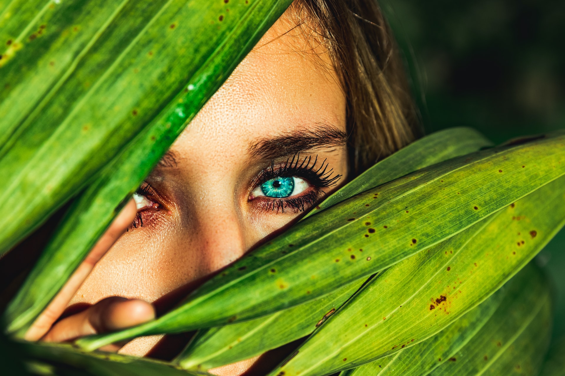 closeup of person's eyes, hiding behind plant leaves, why you need eye cream