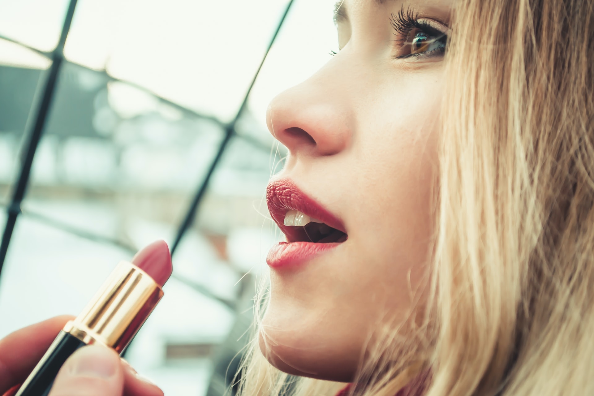 closeup of blonde woman applying lipstick