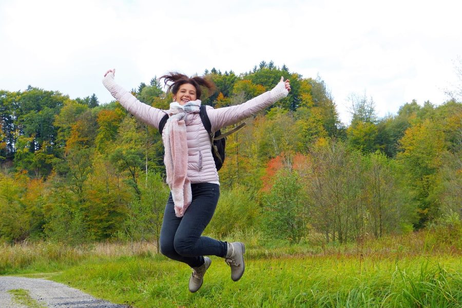 person wrapped up warm for winter outside, jumping in front of trees