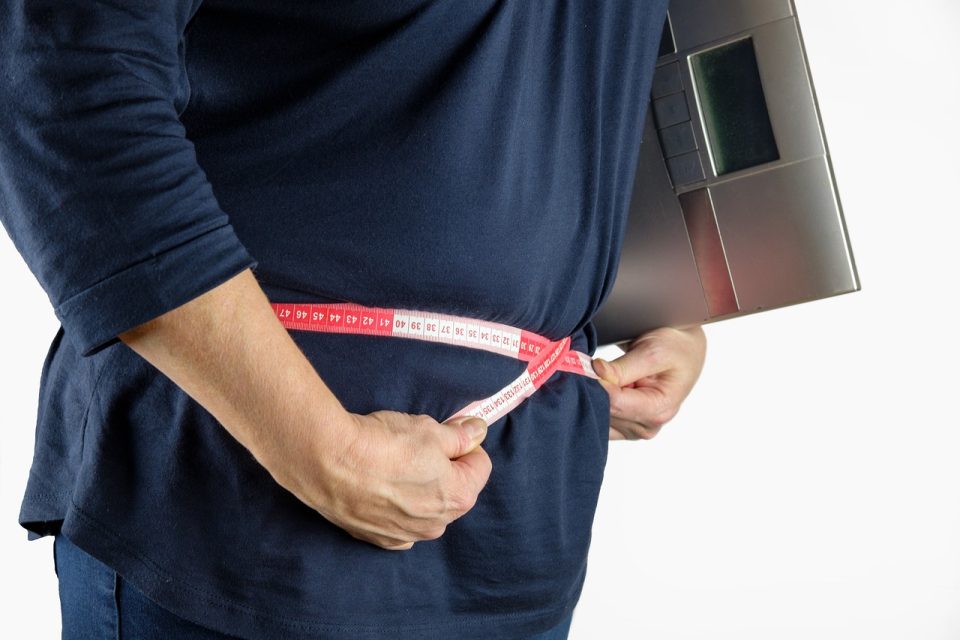 Man measuring his stomach with a measuring tape and holding scales