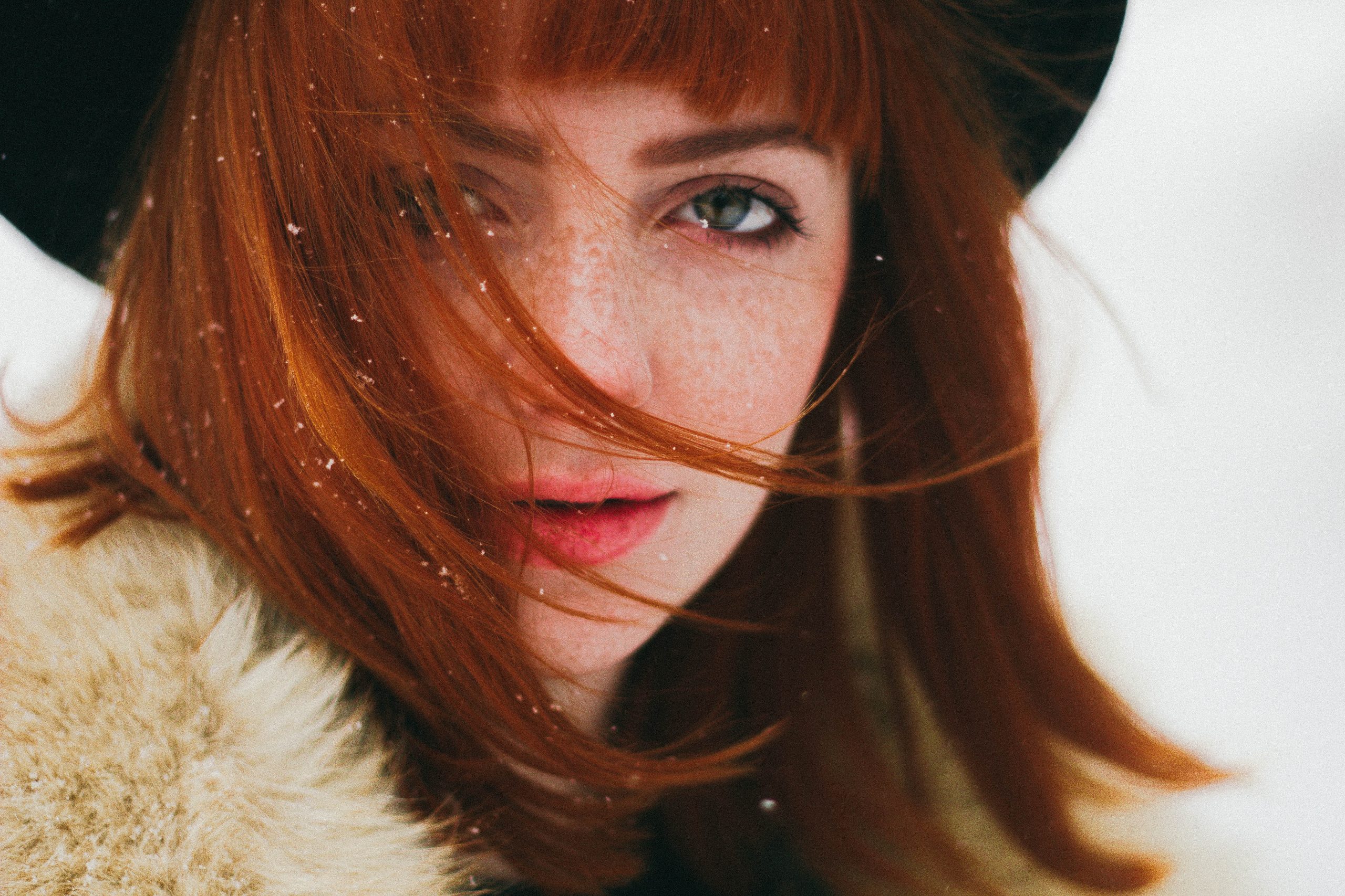 closeup of red-haired model looking at camera, wind blowing hair, wearing furs and hat