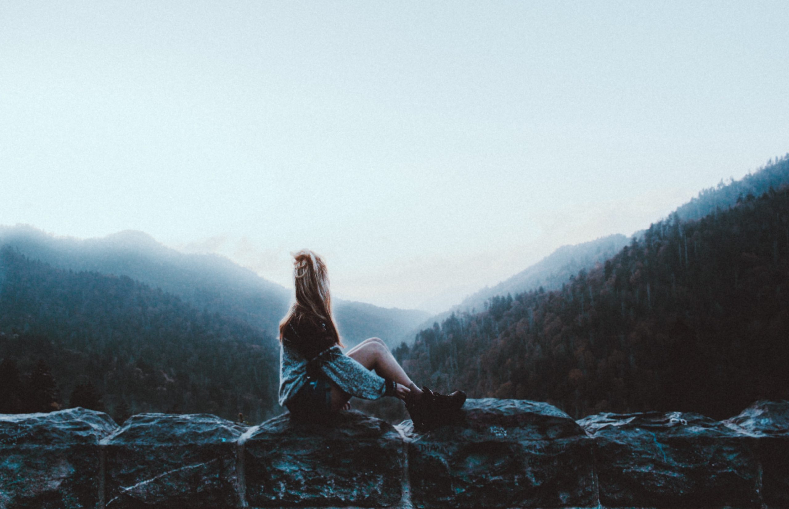 adventurous woman sits on wall looking at mist and mountains