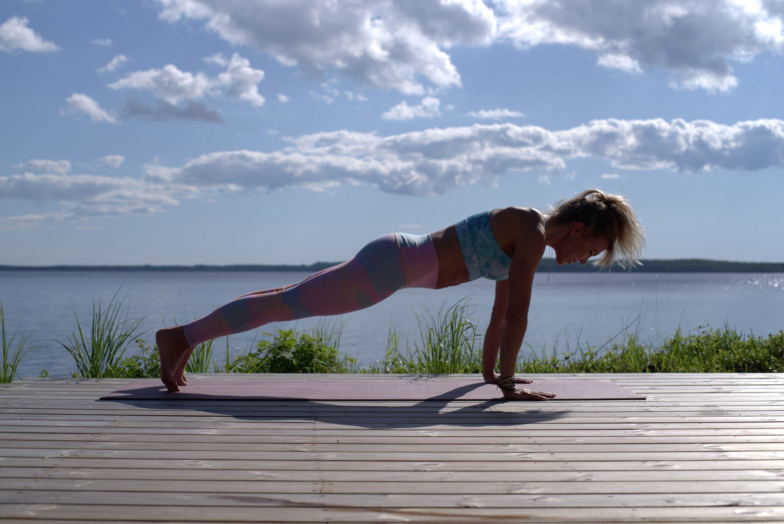 athletic woman in press-up position on boardwalk by lake