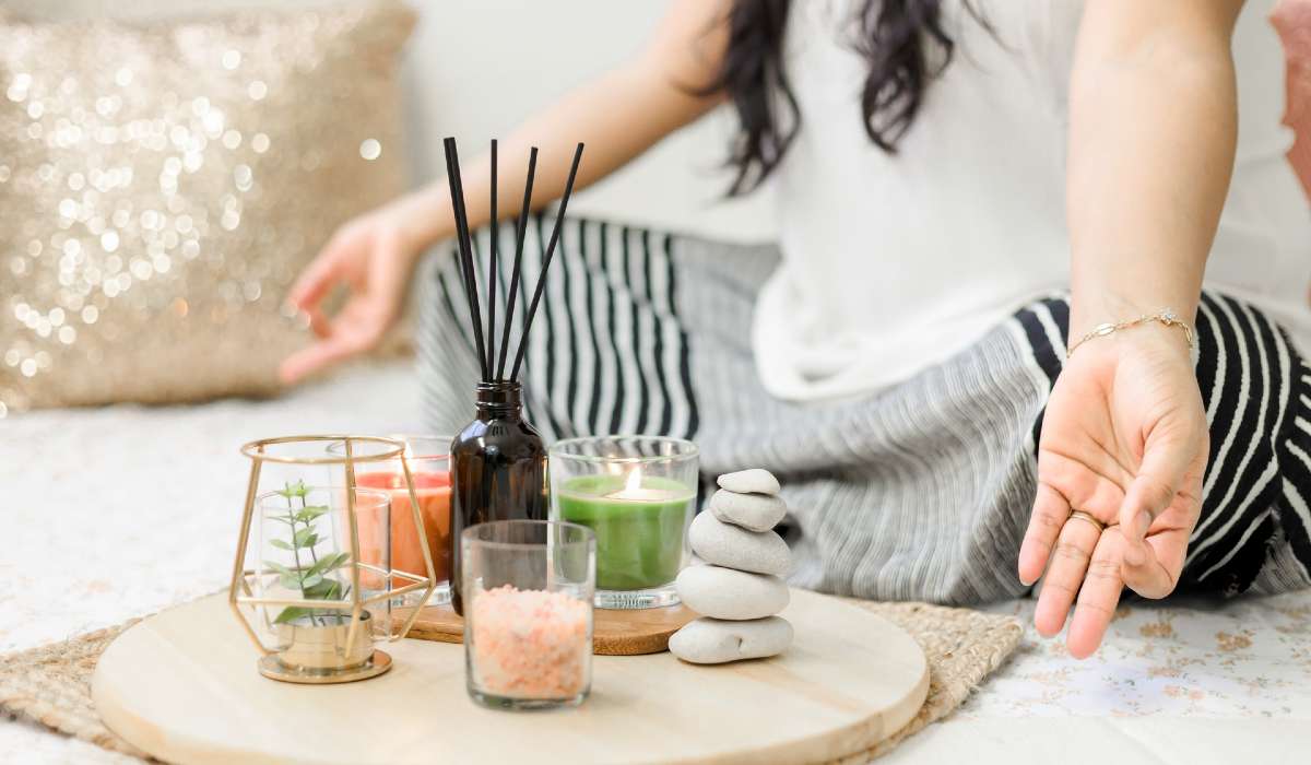 Closeup of person meditating, practicing mindfulness, beside a small circular table with incense, stones and other serene items