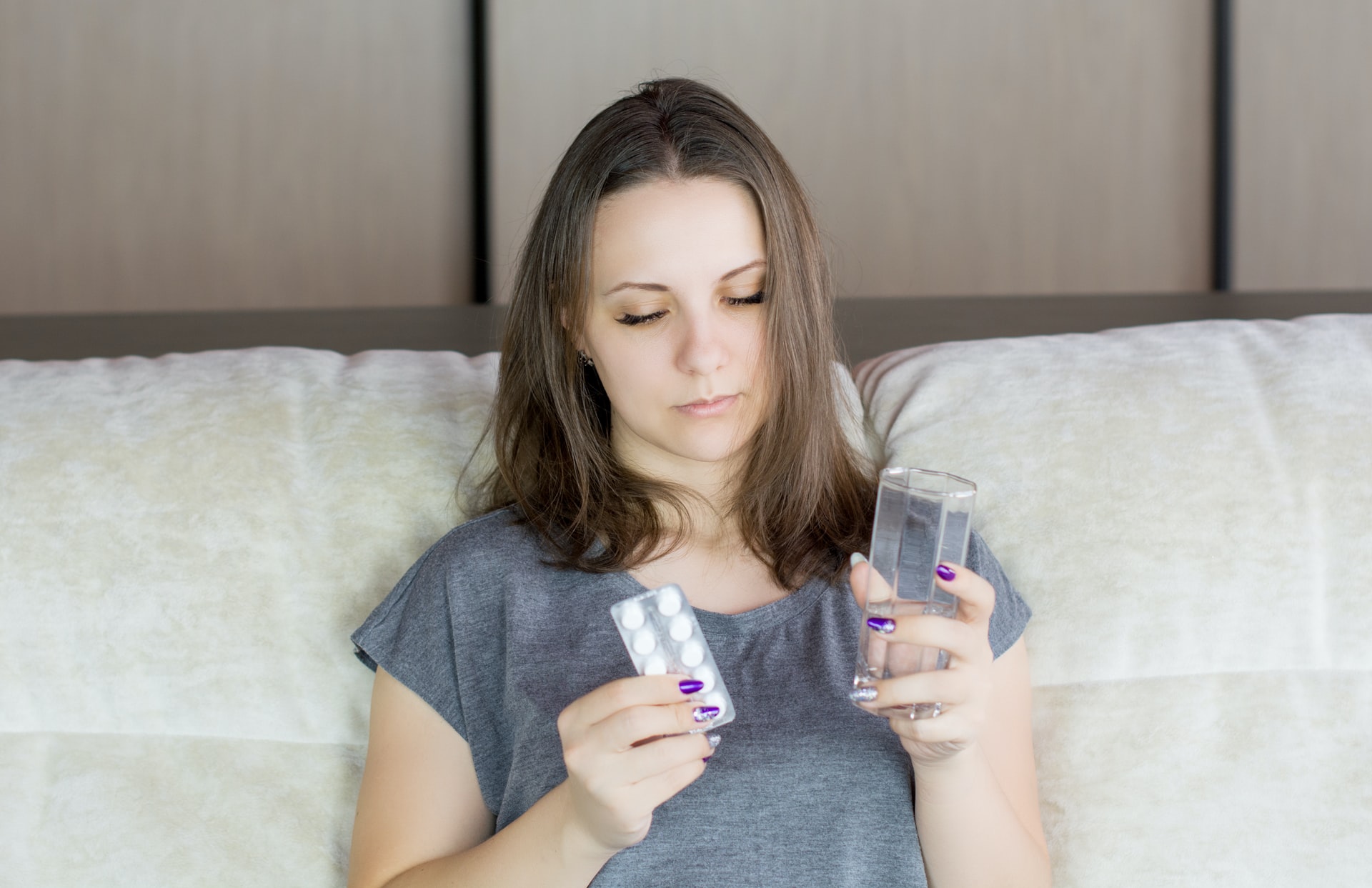 person resting on bed, holding a glass of water in one hand and strip of vitamins in the other