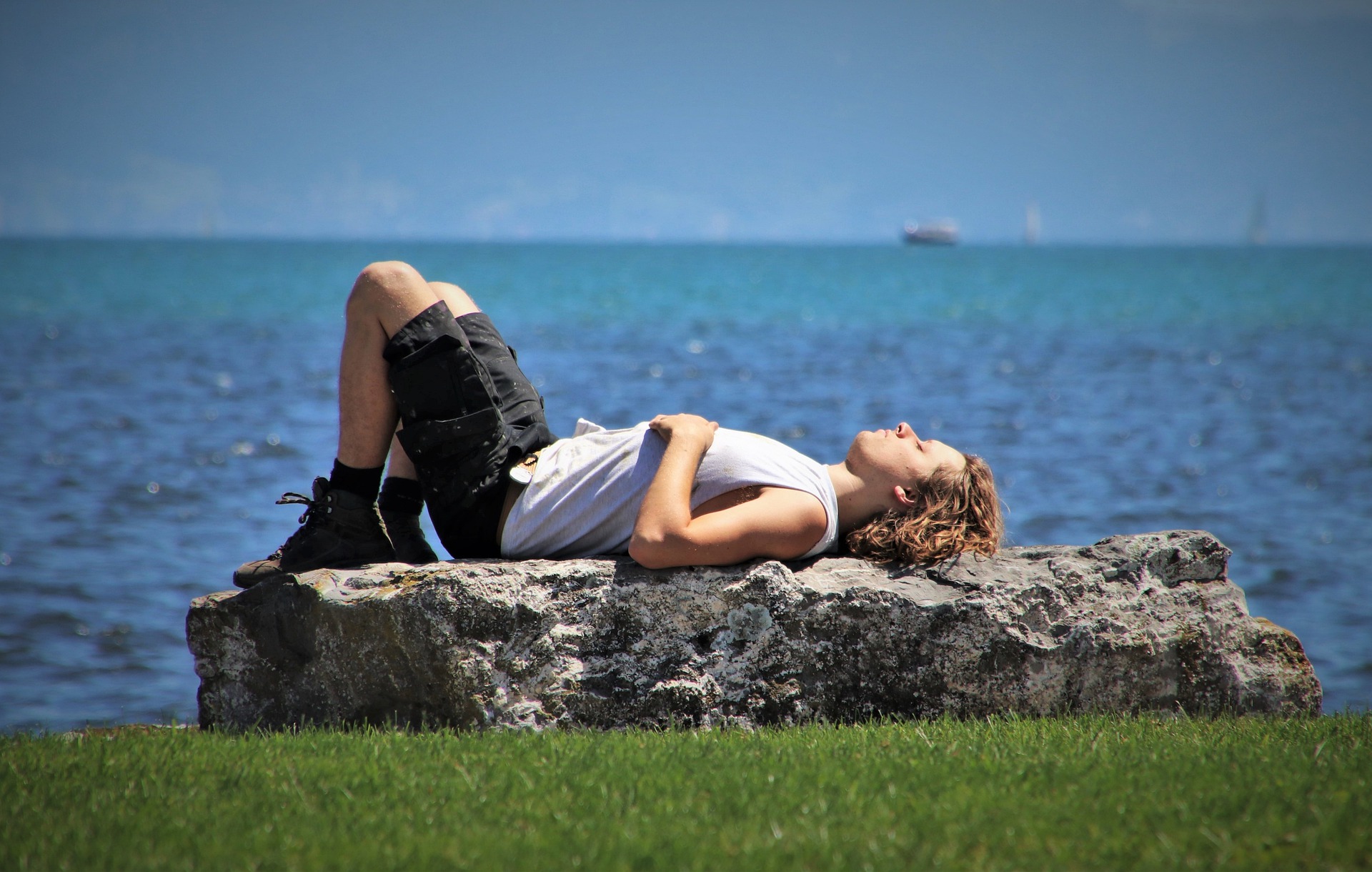 man sunbathing on a rock by water