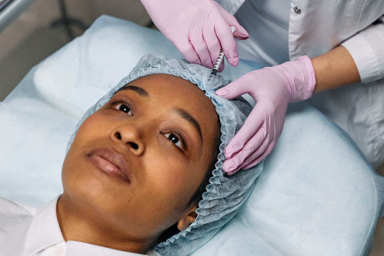 person lying on a surgical bed wearing a hair net, receiving botox injection