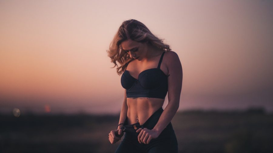 person in great shape stands outside, looking down at toned stomach, admiring weight loss through oversized trousers