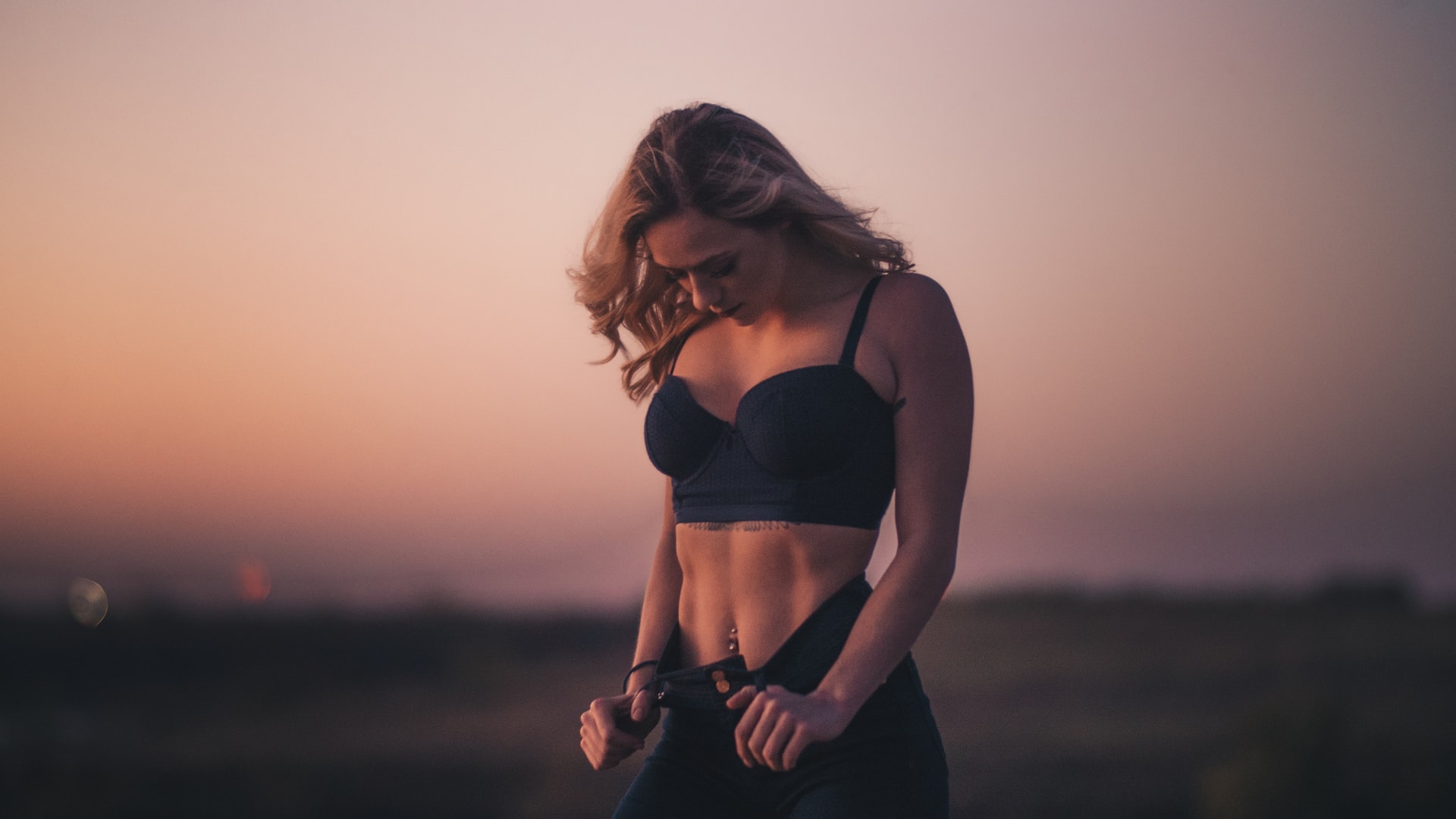 person in great shape stands outside, looking down at toned stomach, admiring weight loss through oversized trousers