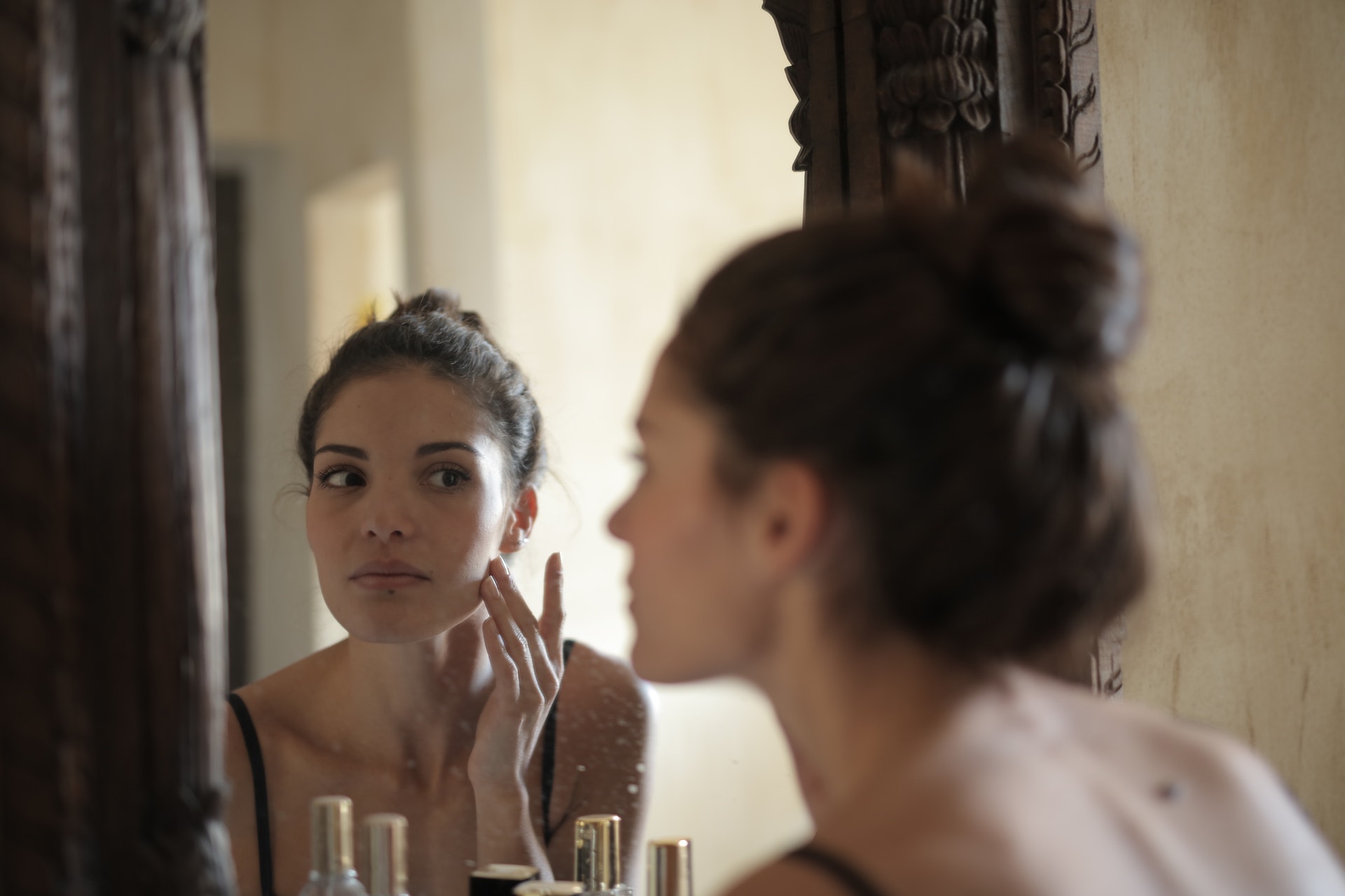 woman touching her cheek, looking in the mirror