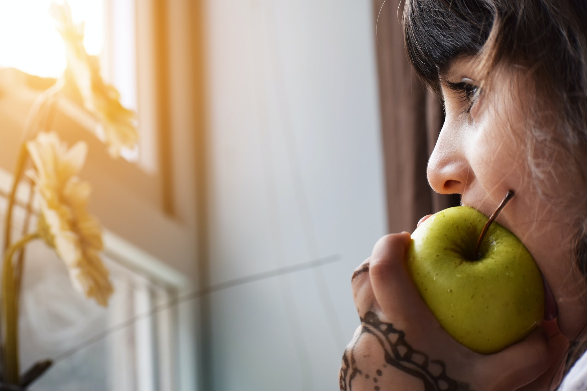 closeup of person taking a bite out of an apple, looking out a window
