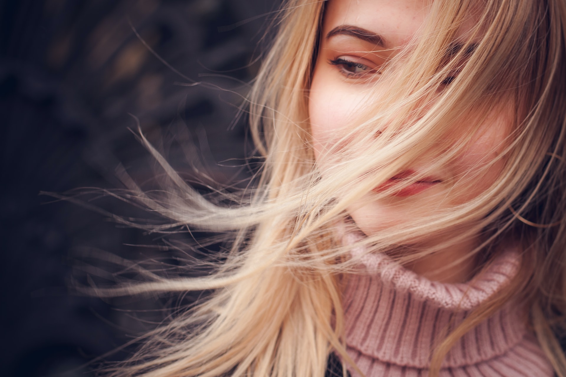 closeup of person's face, blonde hair blowing across cheek, she wears a turtle neck, winter skincare