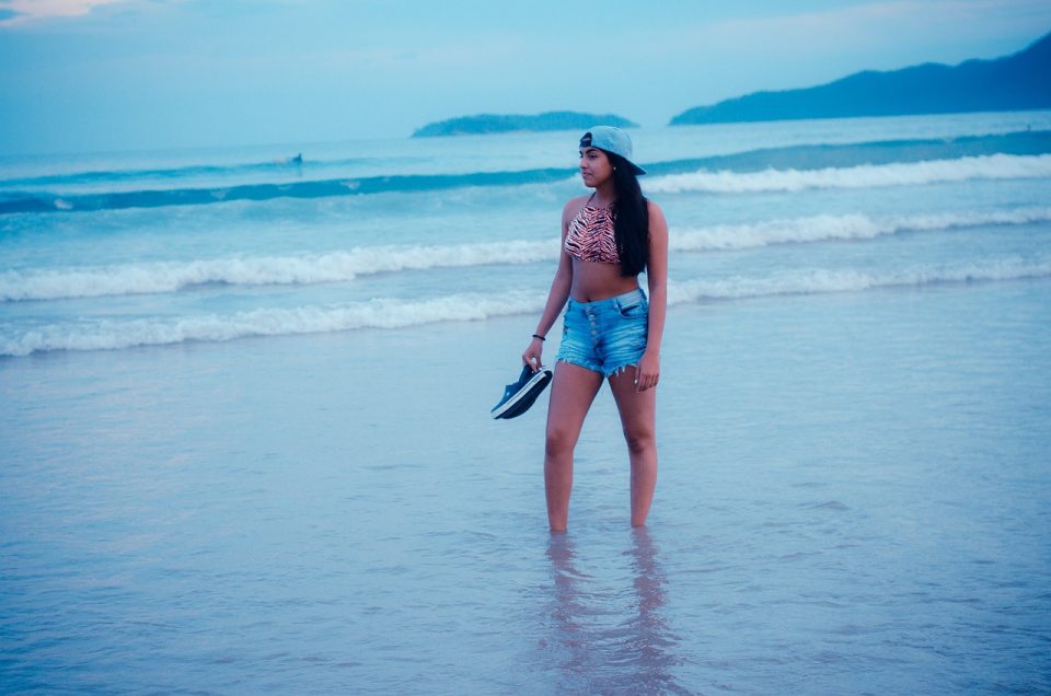 Young woman paddling in the sea holding trainers